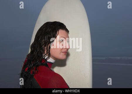 Femme sérieuse surfer avec une planche de surf à la plage au loin Banque D'Images