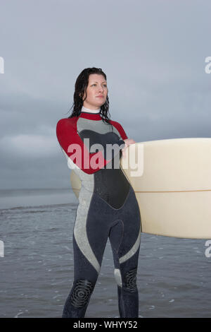 Femme sérieuse surfer avec une planche de surf à la route tout en se tenant dans l'eau à beach Banque D'Images