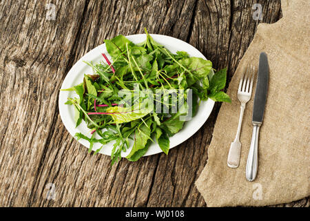 Feuilles de salade verte fraîche saine sur la plaque avec des couverts sur fond de bois rustique. Banque D'Images