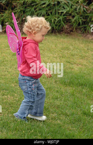 Blondie enfant fille avec des cheveux courts et costume papillon ailes marcher sur l'herbe. Banque D'Images