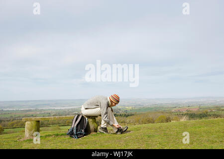 Longueur totale side view of young female hiker attacher sa chaussure sur le banc de parc Banque D'Images