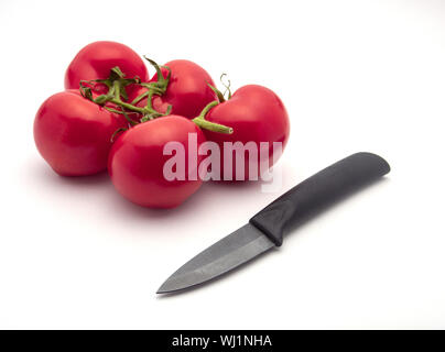 Panicule cinq tomates et un couteau en céramique noir isolé sur fond blanc. Focus sélectif. Banque D'Images