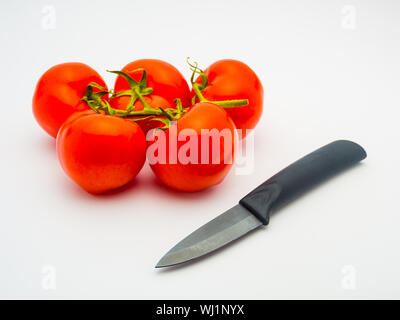 Les tomates rouges frais et un couteau en céramique noir isolé sur fond blanc. Banque D'Images