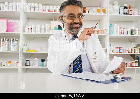 Portrait of a senior homme pharmacien holding prescription avec presse-papiers sur 24 sur le lieu de travail Banque D'Images