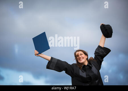 Jolie jeune femme célébrer joyeusement son diplôme - diffusion large ses bras, tenant son diplôme, savourant son succès (tons couleur image ; shal Banque D'Images