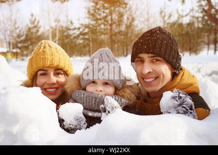 Happy Family joue lutte contre la neige. Maman, fils et papa se cachent derrière des murs avec des boules de neige. Week-end familial dans winter park. Banque D'Images