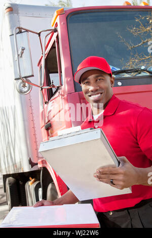 Portrait of a happy African American man holding clipboard avec des camions de livraison en arrière-plan Banque D'Images