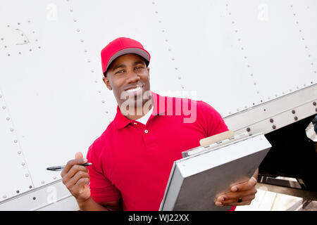 Portrait of a happy African American man holding clipboard avec des camions de livraison en arrière-plan Banque D'Images