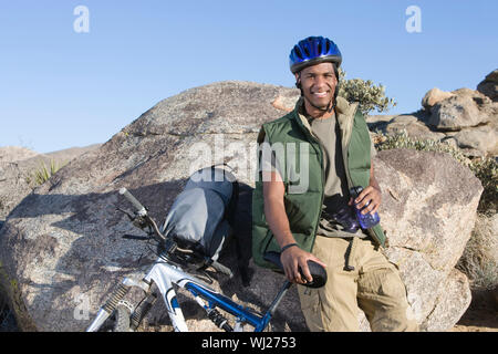 Portrait d'un African American man leaning on rock par cycle tout en tenant la bouteille d'eau Banque D'Images
