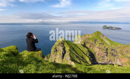 Femme randonneur regardant le coucher du soleil sur les falaises des îles Vestmann (Heimaey - sud de l'Islande) Banque D'Images