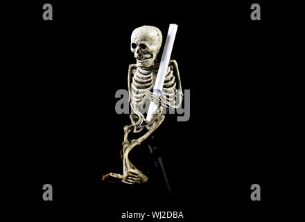La squelette de caoutchouc tenant un cigare , isolé sur fond noir , image conceptuelle au sujet de questions liées à la santé des fumeurs. Banque D'Images