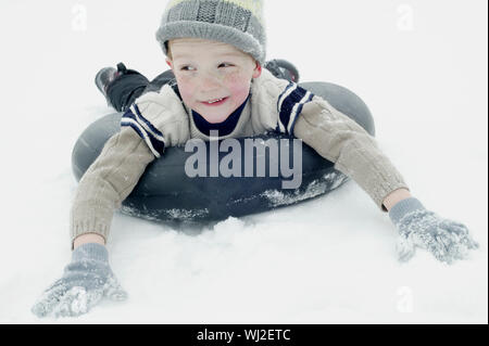Happy Young boy en vêtements d'hiver la luge sur snow tube Banque D'Images