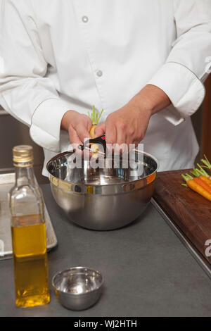 Portrait male chef peeling les carottes dans un bol à mélanger au comptoir de la cuisine Banque D'Images