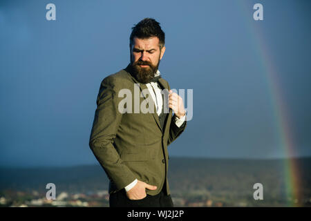 Homme avec barbe et moustache et paysage avec arc-en-ciel sur l'arrière-plan. Hipster avec élégance en face de ciel dramatique avec arc-en-ciel. Guy avec st Banque D'Images