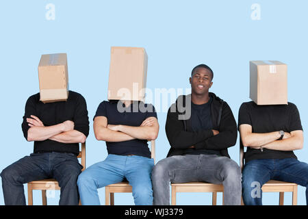 Avec des amis de l'homme visage couvert avec des boîtes en carton, assis sur des chaises sur fond bleu Banque D'Images