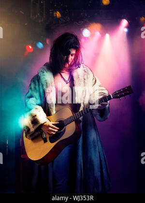 Jeune musicien de rock en manteau de fourrure à jouer de la guitare à concert Banque D'Images
