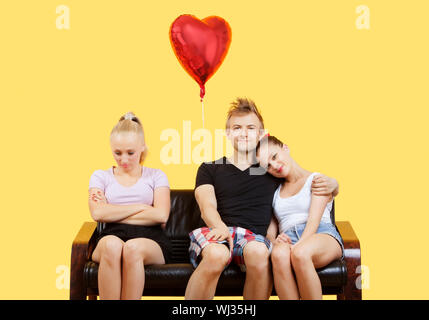 Portrait of young couple sitting on sofa with female friend sentiment laissé sur fond jaune Banque D'Images