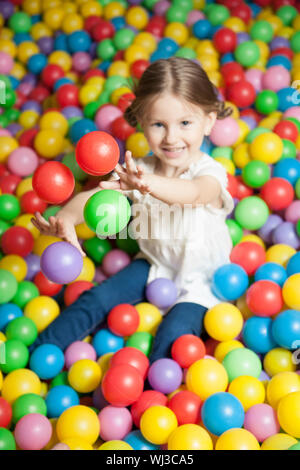 Jeune fille en piscine à balles de lancer des balles de couleur Banque D'Images