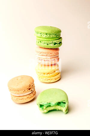 Détail de délicieux marron, vert et jaune de macarons empilés dans un tas sur un fond blanc, à côté d'un morceau de gâteau vert mordu des mensonges. Banque D'Images