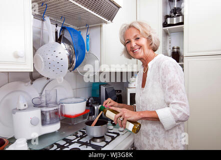 Portrait of senior woman ajout d'huile d'olive dans la casserole au comptoir de la cuisine Banque D'Images