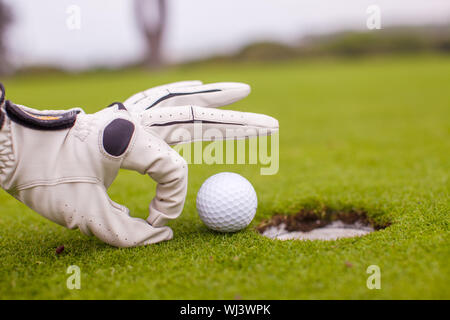 Close-up of a man's hand putting balle de golf dans le trou en cours Banque D'Images