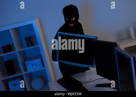Homme vêtu de noir et portait un passe-montagne est de voler un ordinateur portable à partir d'un bureau Banque D'Images