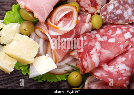 Arrangement des épiceries fines de charcuterie avec jambon fumé, différentes saucisses, fromage délicieux et olives vertes sur fond de bois foncé gros plan Banque D'Images