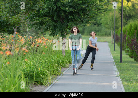 Le patin à roues alignées et les femmes équitation pousser scooter sur sentier du parc Banque D'Images