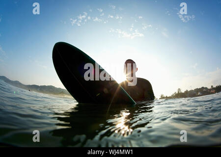 Mâle Silhouette chevauchant surfeur surf dans l'océan ensoleillé Banque D'Images