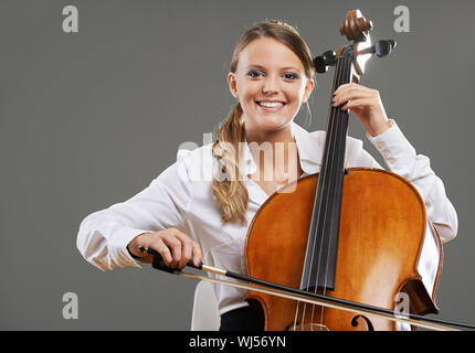 Souriante jeune femme violoncelliste sur fond gris Banque D'Images