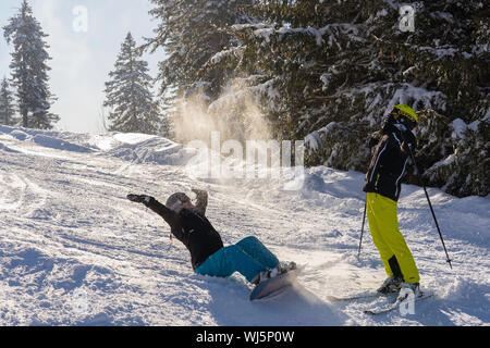 Les adolescents s'asseoir avec le snowboard dans la neige poudreuse heureux et se jette dans l'air, boy stands avec du ski sur la montagne et cheers joyeusement dans le s Banque D'Images