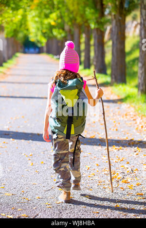 Randonnées kid girl avec bâton de marche et sac à dos vue arrière à l'automne la voie et pantalon camouflage Banque D'Images