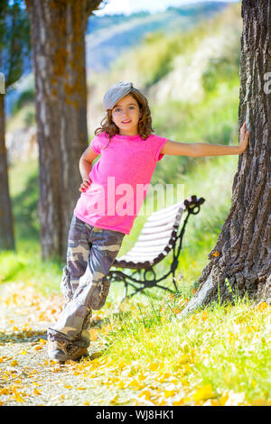 Kid girl avec pantalon camouflage et capuchon en banc de parc piscine avec tshirt rose Banque D'Images