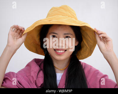 Jolie fille thaïe pose pour la caméra avec une disquette jaune hat. Banque D'Images