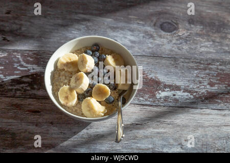 Un bol de porridge d'avoine garnie de tranches de banane et de bleuets. Le bol est sur un fond de bois rustique permettant à beaucoup de l'exemplaire de l'espace. Banque D'Images