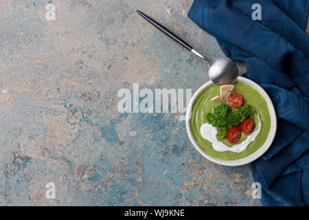 Set de table avec la soupe crème de brocoli, avec cuillère et serviette bleue sur fond de béton. Harvest food, haut Vue, télévision lay Banque D'Images