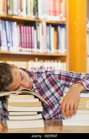 Épuisé handsome student resting head on piles de livres dans la bibliothèque Banque D'Images