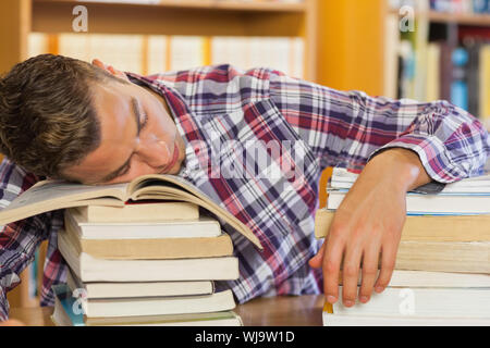 Fatigué handsome student resting head on piles de livres dans la bibliothèque Banque D'Images