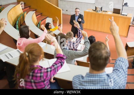 Vue arrière d'étudiants augmentant les mains avec un enseignant dans la salle de conférence du Collège Banque D'Images