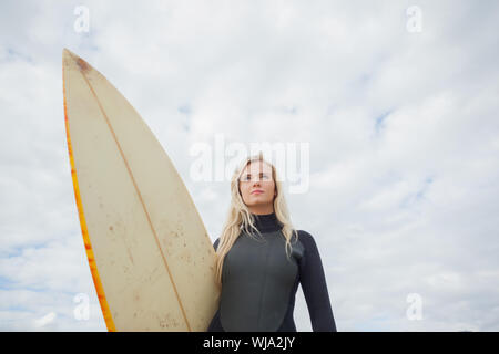 Low angle view of a beautiful young woman with surfboard contre ciel nuageux Banque D'Images