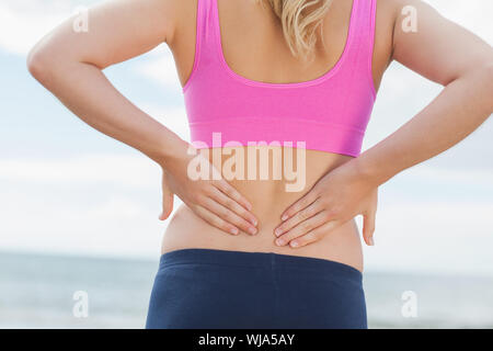 Close up mid section d'une femme en bonne santé dans les sports bra souffrant de maux de dos on beach Banque D'Images