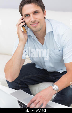 Portrait de l'homme à l'aide d'ordinateur portable et téléphone portable à la maison Banque D'Images
