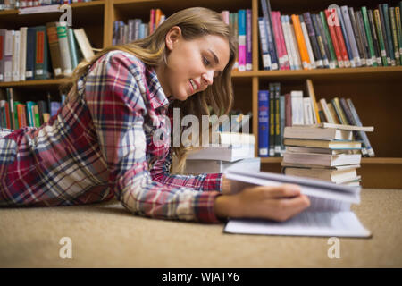 Smiling student lying on library floor reading Banque D'Images