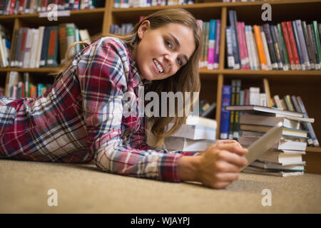 Smiling student lying on floor using tablet pc de la bibliothèque Banque D'Images