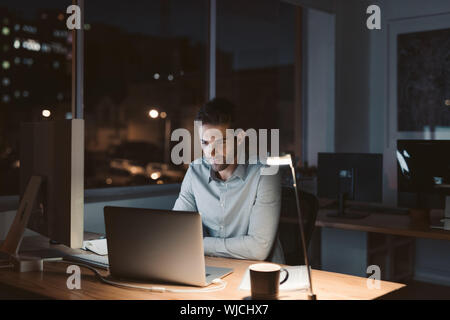 Jeune homme d'affaires travaillant tard dans la nuit dans un bureau Banque D'Images