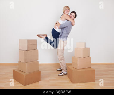 Happy young couple dans une étroite étreinte extatique sourire heureux tels qu'ils sont entourés de cartons dans leur nouvelle maison