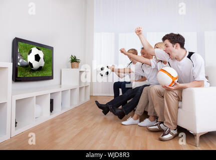 Famille jubilatoire à regarder la télévision comme ils encourager leurs home côte dans une compétition sportive Banque D'Images