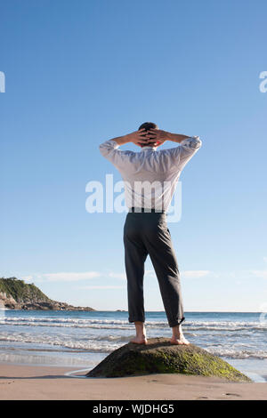 Businessman standing pieds nus sur un rocher au bord de la mer Banque D'Images