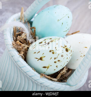 Trois teintes bleu naturel oeufs de Pâques dans un panier avec une seule plume d'oiseau pour une célébration saisonnière rustique symbolique de la résurrection du Christ Banque D'Images