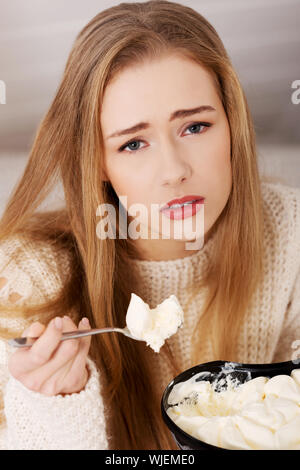 Triste, inquiet Beautiful woman eating ice cream. Contexte à l'intérieur. Banque D'Images